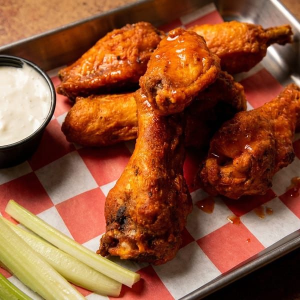 Spicy chicken wings, celery, and ranch dip on a metal tray with checkered paper.