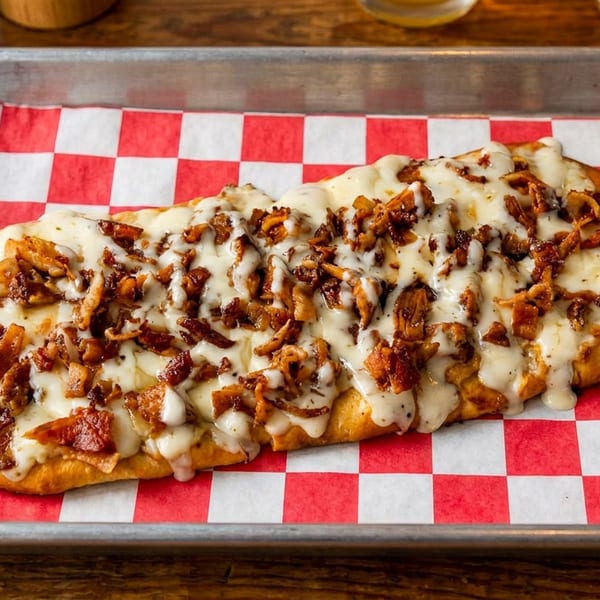 Flatbread with melted cheese and crispy bacon bits on a checkered paper-lined tray.